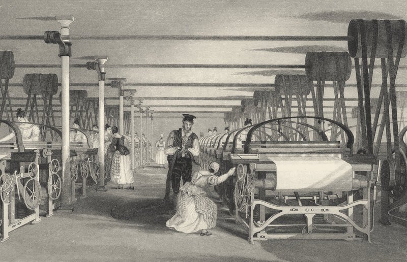 Engraving of a long weaving shed lined with power looms. Women tend the looms and an overseer stands in the aisle. Overhead, rows of shafts and drums carry leather belts down to every loom.